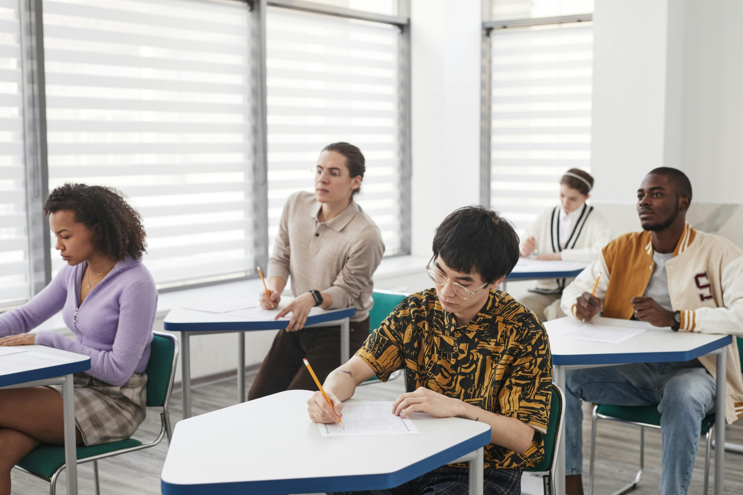 A diverse group of students writing exam papers in a well-lit classroom environment.